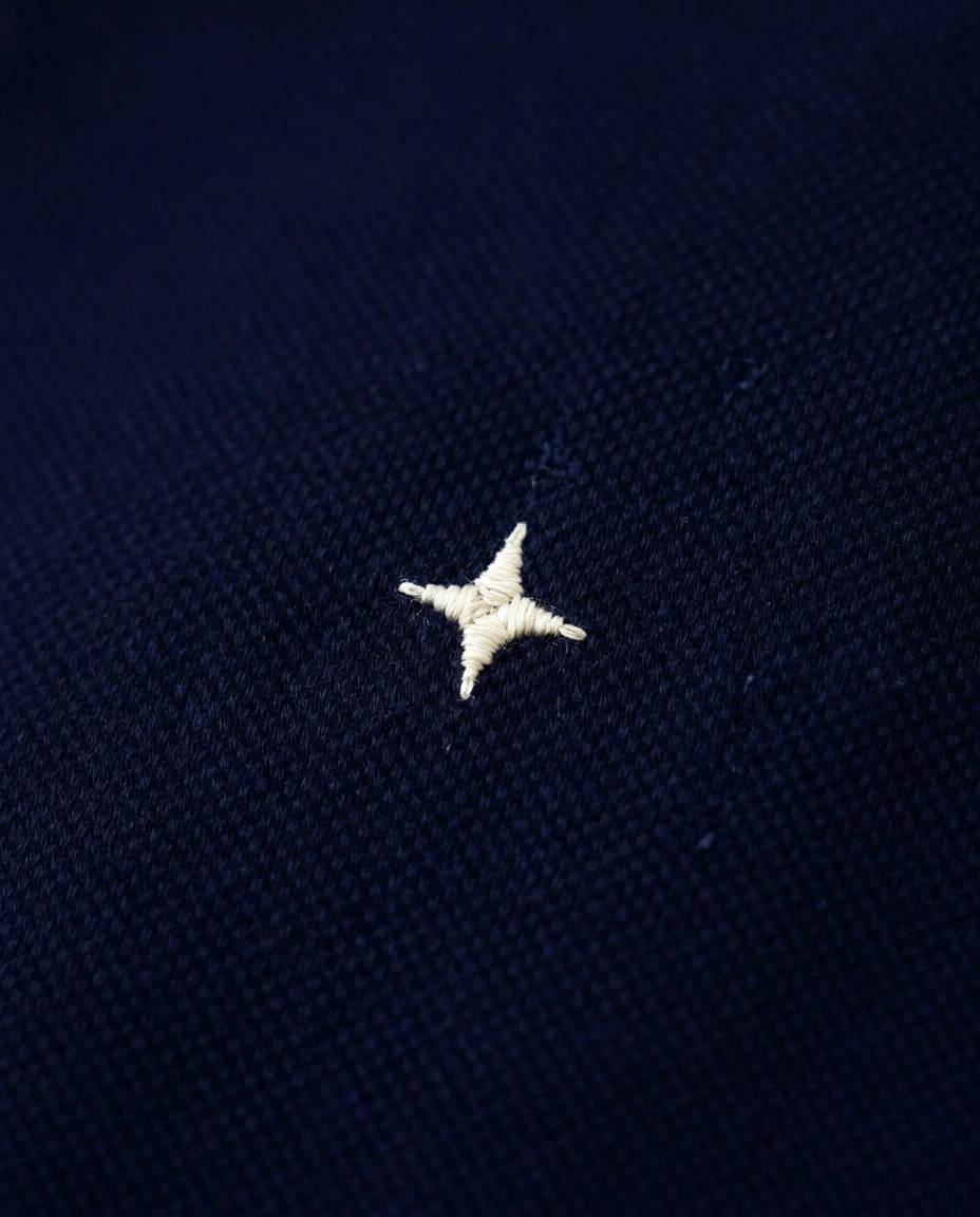 Macro detail of the ivory glint embroidered on navy pique cotton